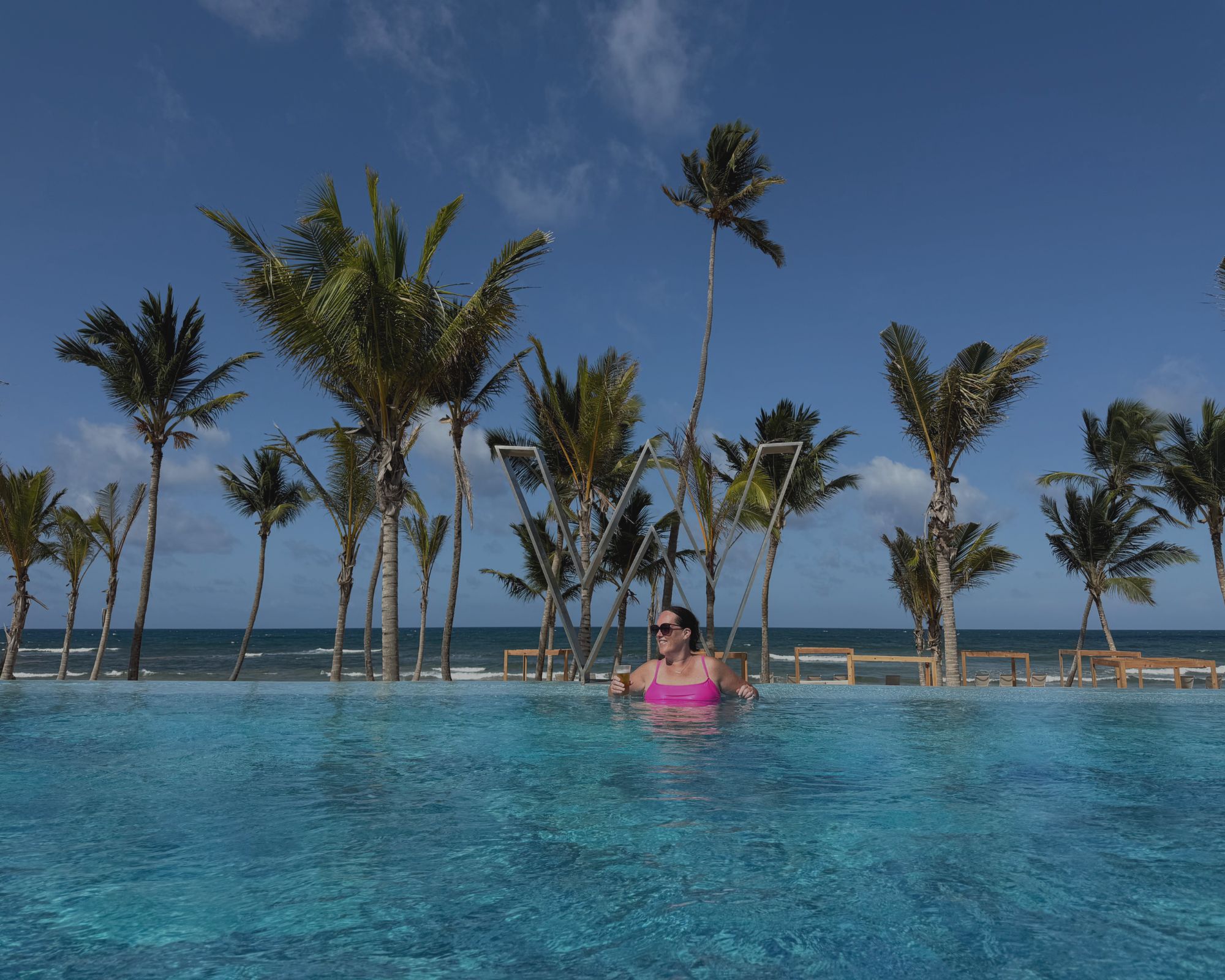 Traveler relaxing in the pool at W Punta Cana with the resort’s iconic illuminated W sign in the background.