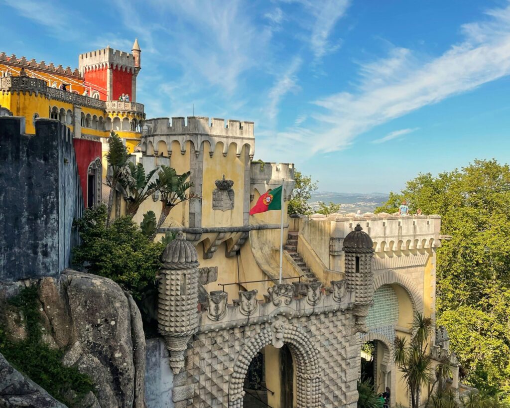 Colorful hilltop palace in Sintra, Portugal surrounded by lush forest and misty mountain views.