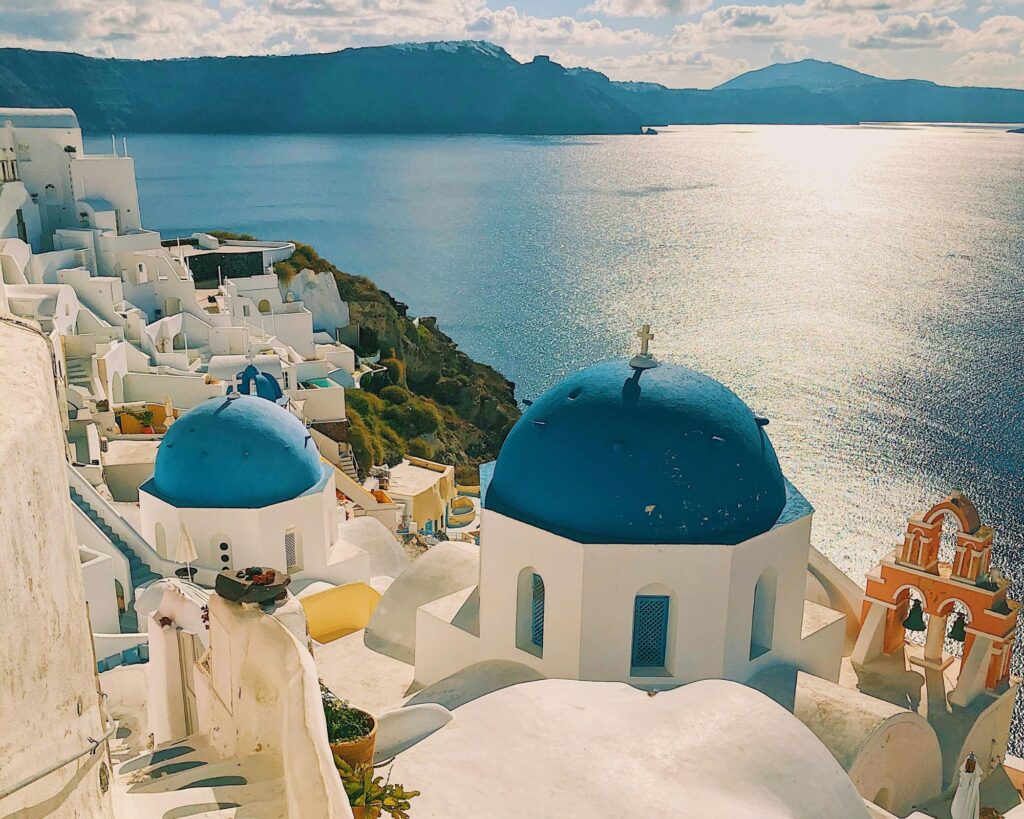 Whitewashed buildings and blue‑domed churches overlooking the caldera at sunset in Santorini, Greece.