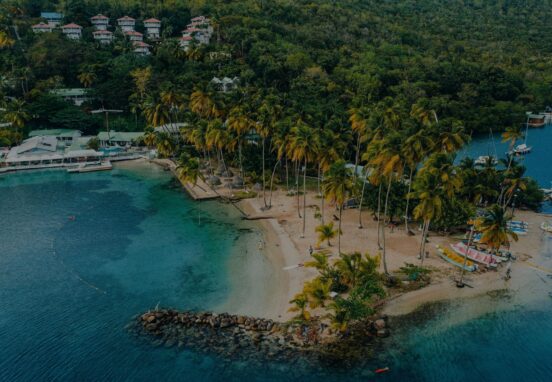 Aerial view of Marigot Bay in St. Lucia with turquoise water, palm trees, and anchored sailboats.