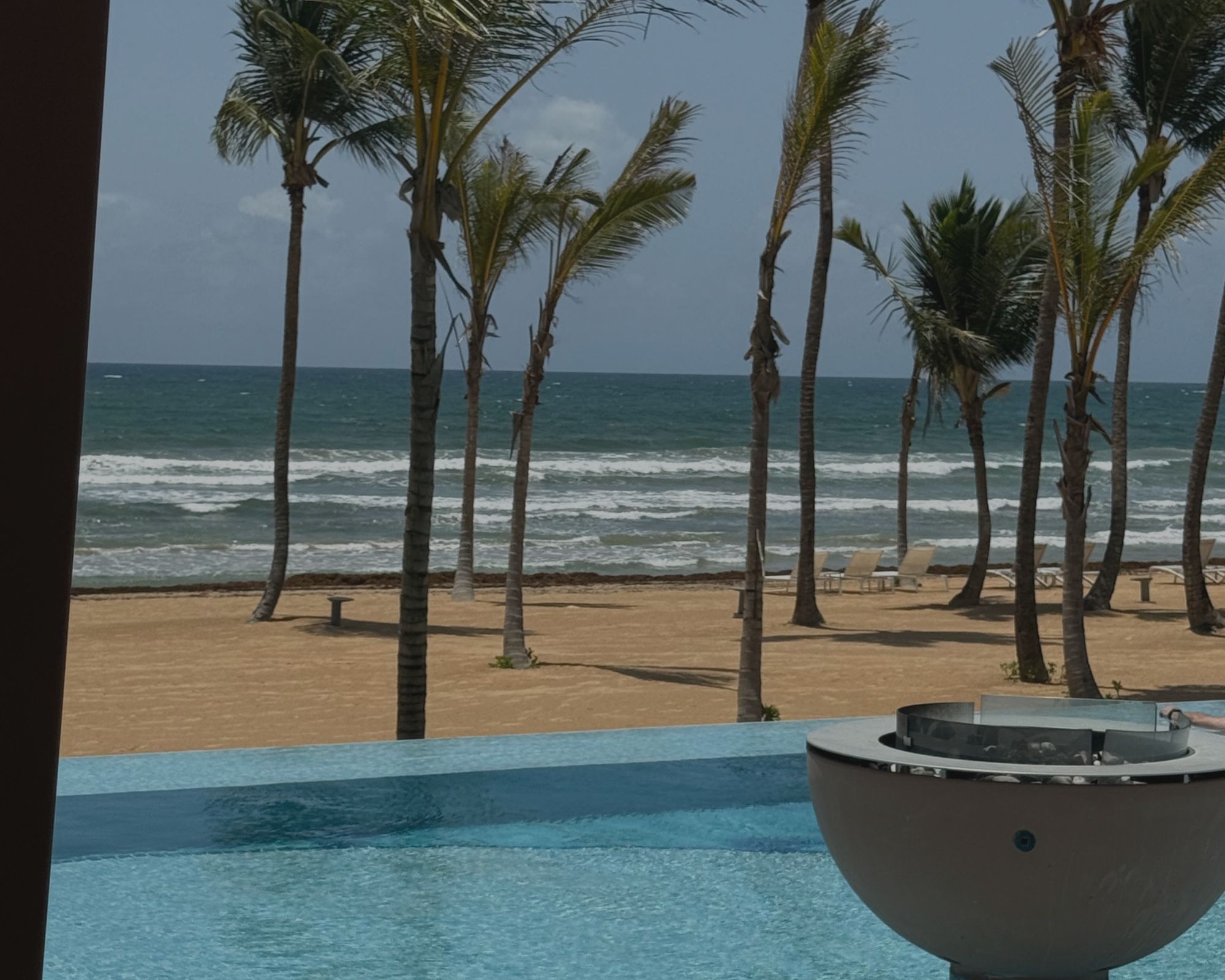 Fire pit built into a resort pool with ocean views and a sandy beach in the background.